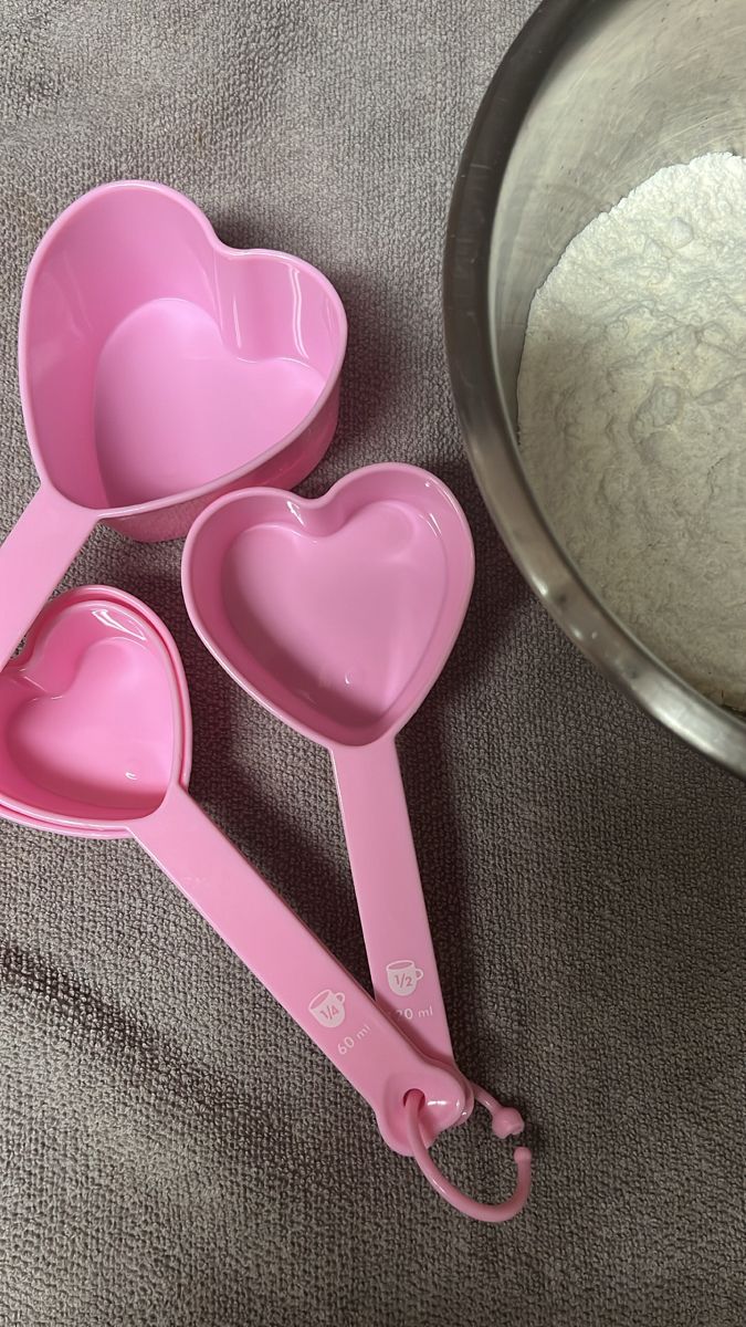 three pink heart shaped measuring spoons next to a bowl