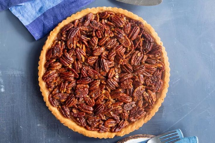 a pecan pie sitting on top of a table next to a knife and fork