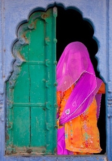 a woman in an orange and pink sari standing at the entrance to a blue building