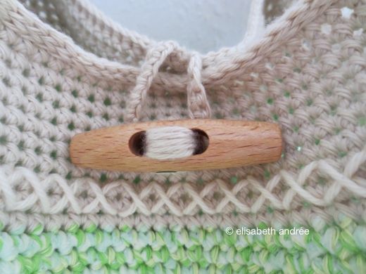 a close up of a knitted sweater with a wooden button in the center and green yarn on the bottom