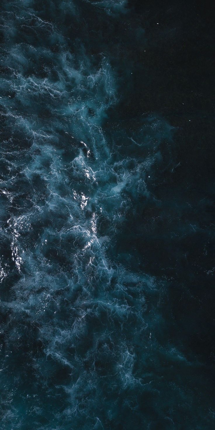 an aerial view of the ocean with dark blue water and white foamy waves in the foreground