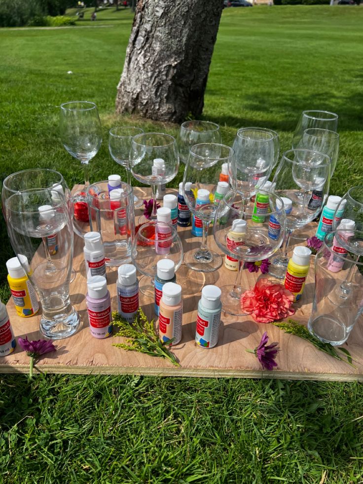 many empty wine glasses and bottles on a wooden table in the grass near a tree