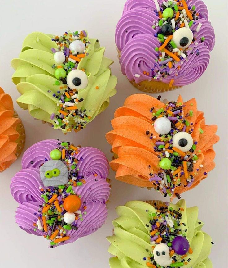 four cupcakes decorated to look like monsters with sprinkles