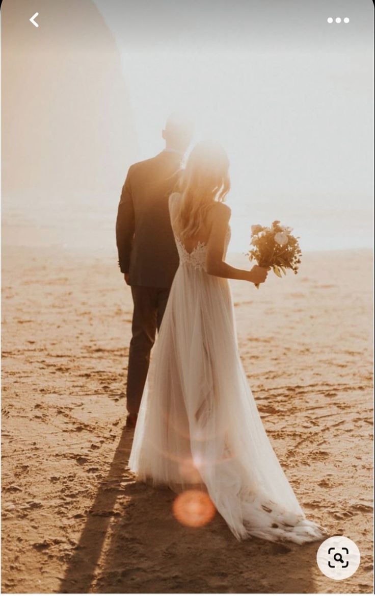 a bride and groom walking on the beach at sunset with their back to the camera