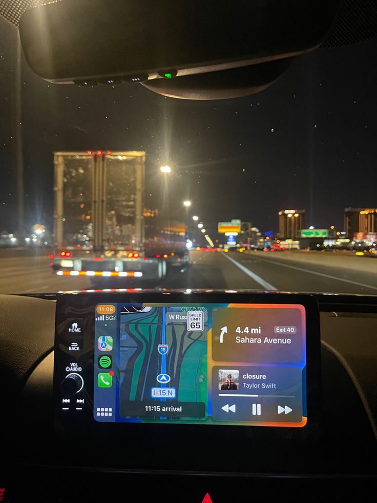 the dashboard of a car with an electronic device on it's display in front of a cityscape at night