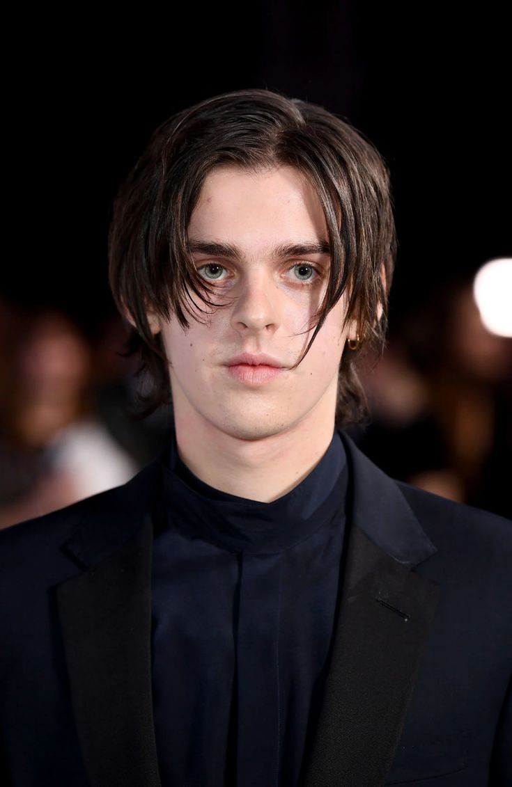 a young man in a black suit and tie looking at the camera with an intense look on his face