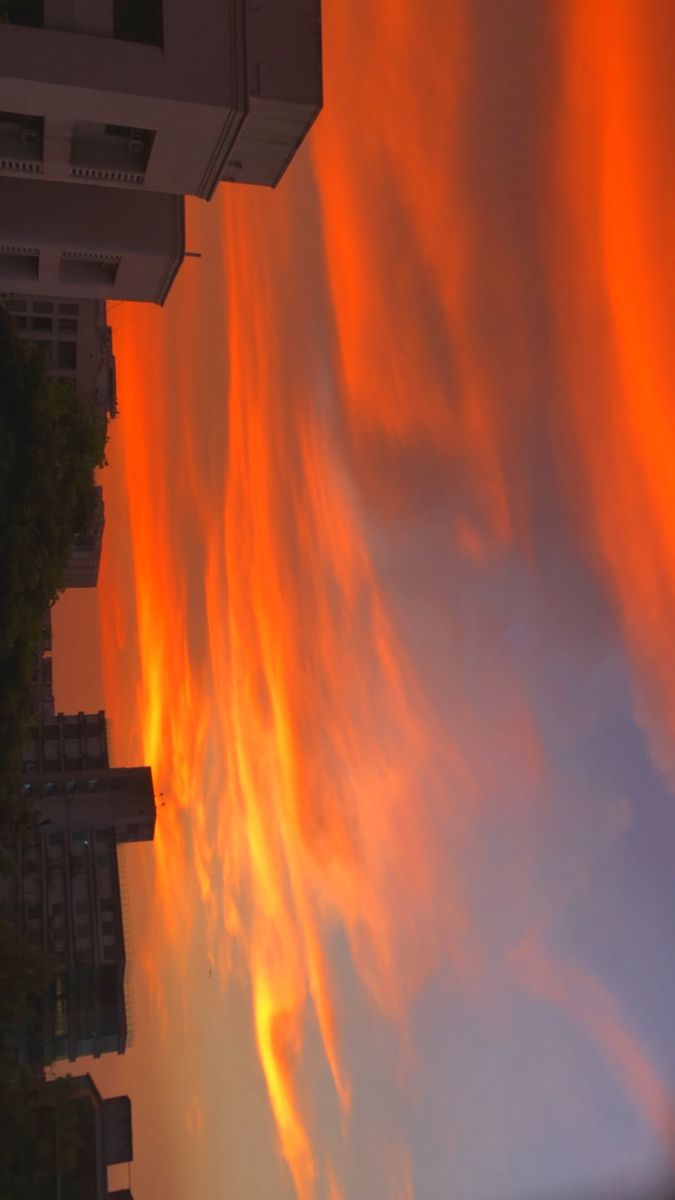 an orange sky with clouds and buildings in the background