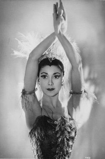 an old black and white photo of a woman with feathers on her head, holding her hands up in the air