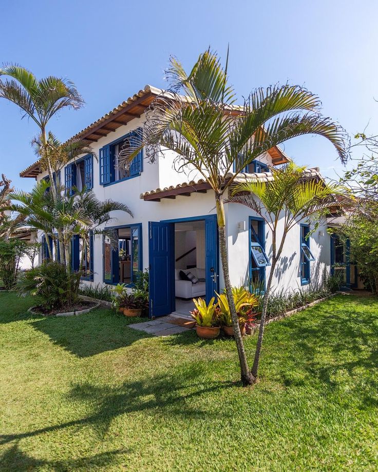 a white house with blue shutters and palm trees in the front yard on a sunny day