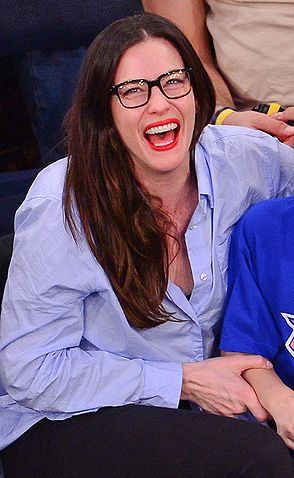 a woman sitting next to a man in a blue shirt and black pants at a basketball game