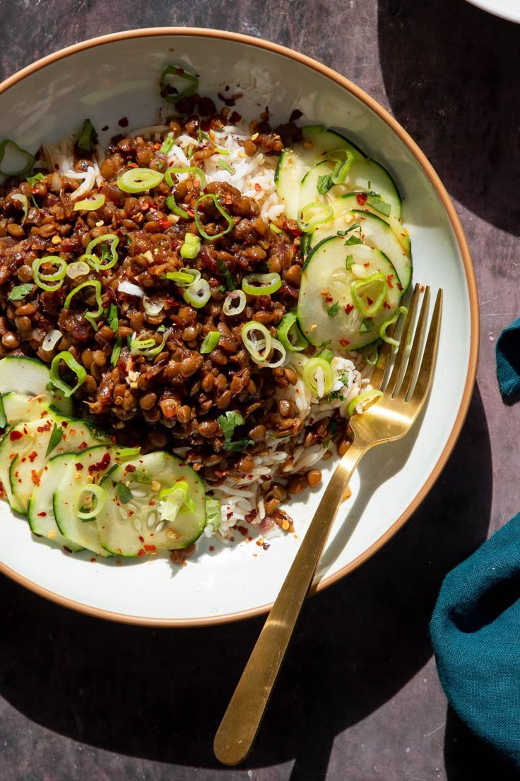 a white plate topped with meat and cucumbers next to a fork on top of a table