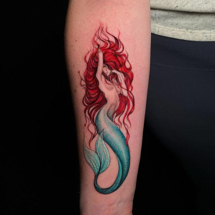 a woman's arm with a red and blue mermaid tattoo on her left arm