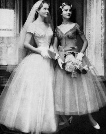 two women in dresses standing next to each other wearing veils and holding bouquets