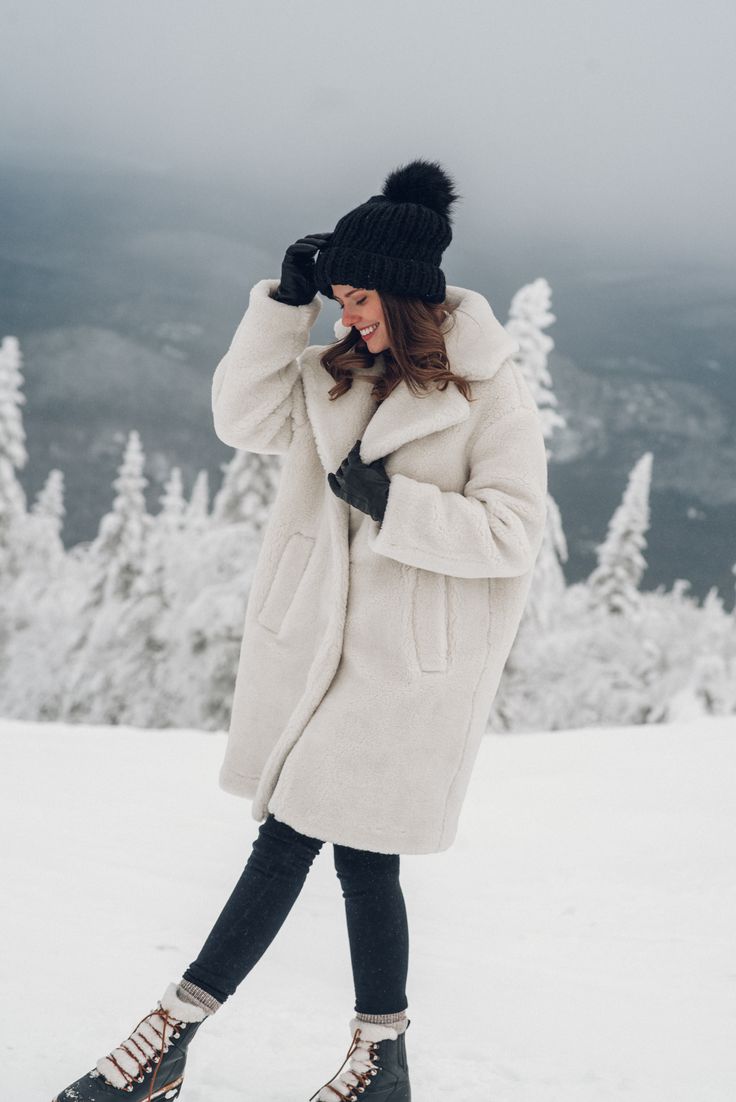 a woman is standing in the snow talking on her cell phone while wearing a white coat and black hat