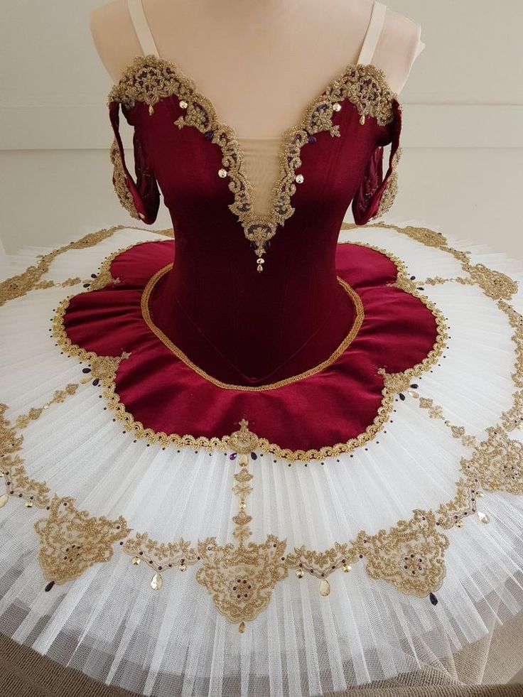 a red and white ball gown with gold trimmings on the bust, sitting on top of a mannequin