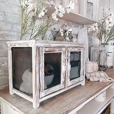 an old white microwave sitting on top of a wooden table with flowers in the window