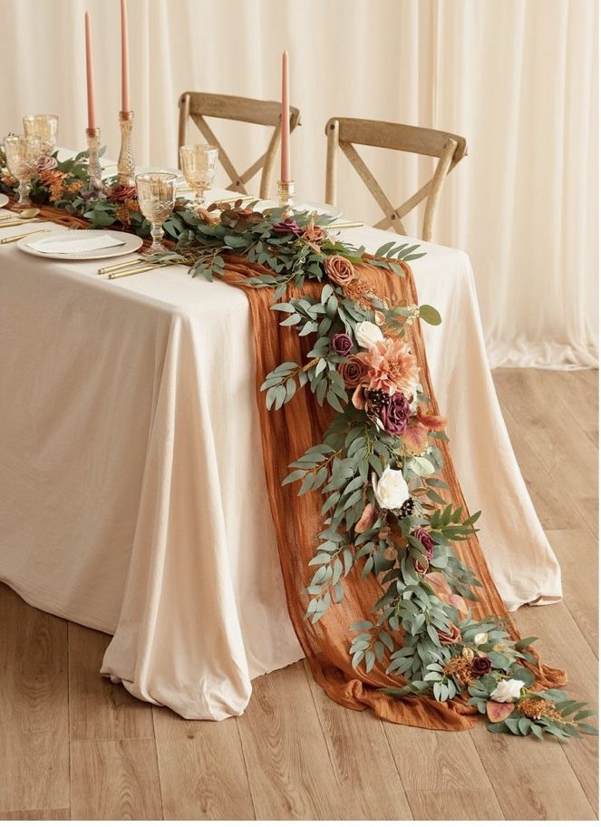 the table is set with an orange runner and flowers on it, along with candles