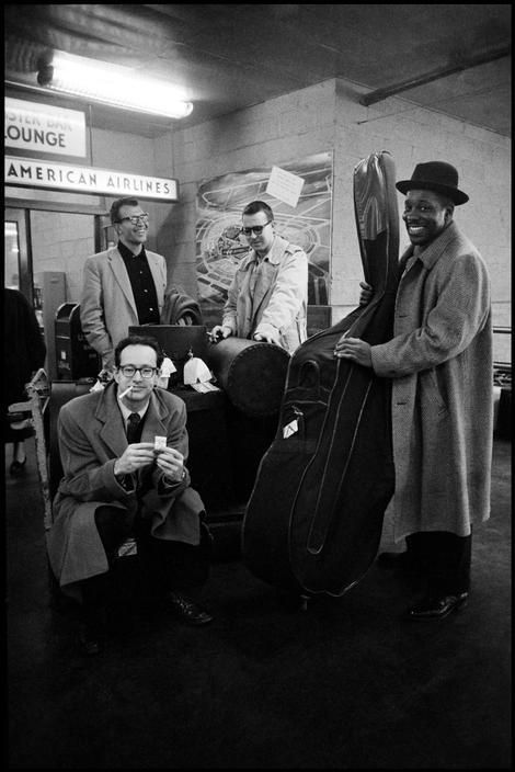 a group of men standing next to each other with luggage in front of them and one man holding a cell phone