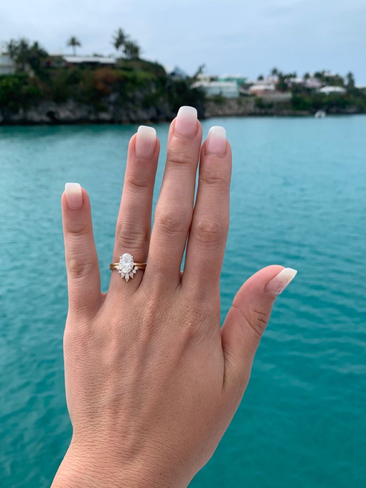 a woman's hand with a ring on her finger near the water and houses in the background