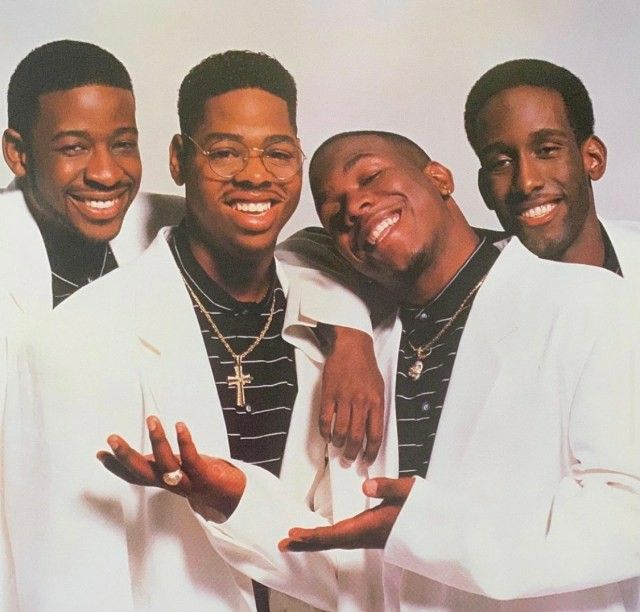 three black men in white suits posing for a photo with one holding his arm around the other's shoulder