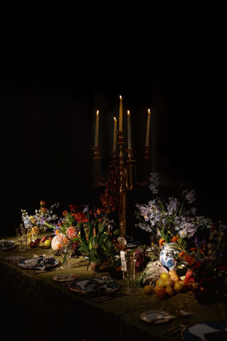 a table with candles and flowers on it in the middle of a dark room filled with plates