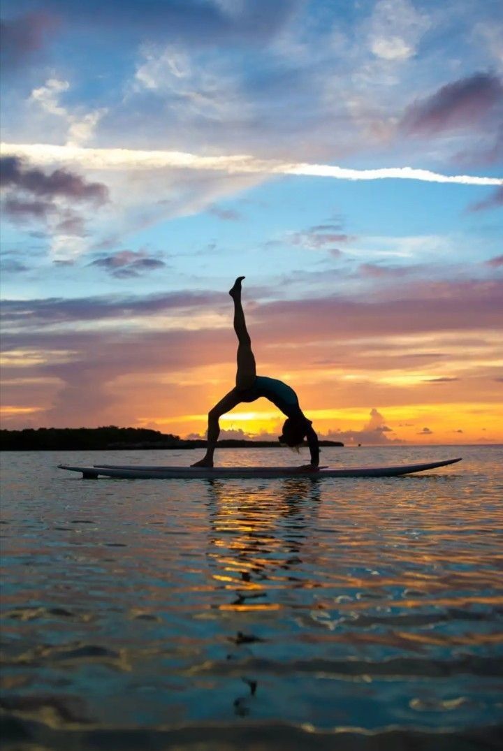 a person on a surfboard doing a handstand in the water at sunset