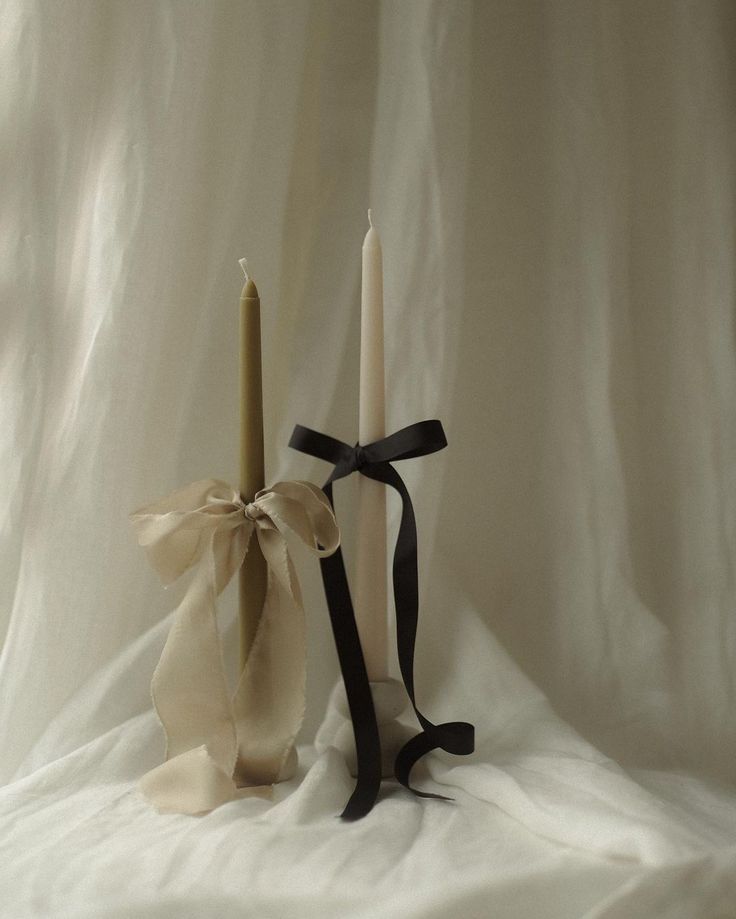 two candles with ribbons tied around them on a white background