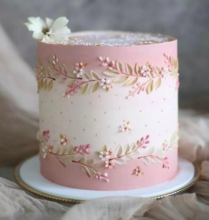 a pink and white cake with flowers on it's top is sitting on a plate