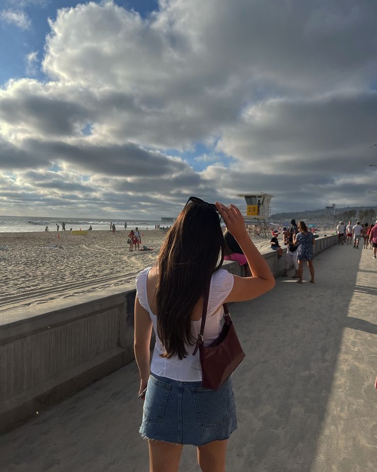 a woman is standing on the beach looking at something in the sky with her hand up to her head