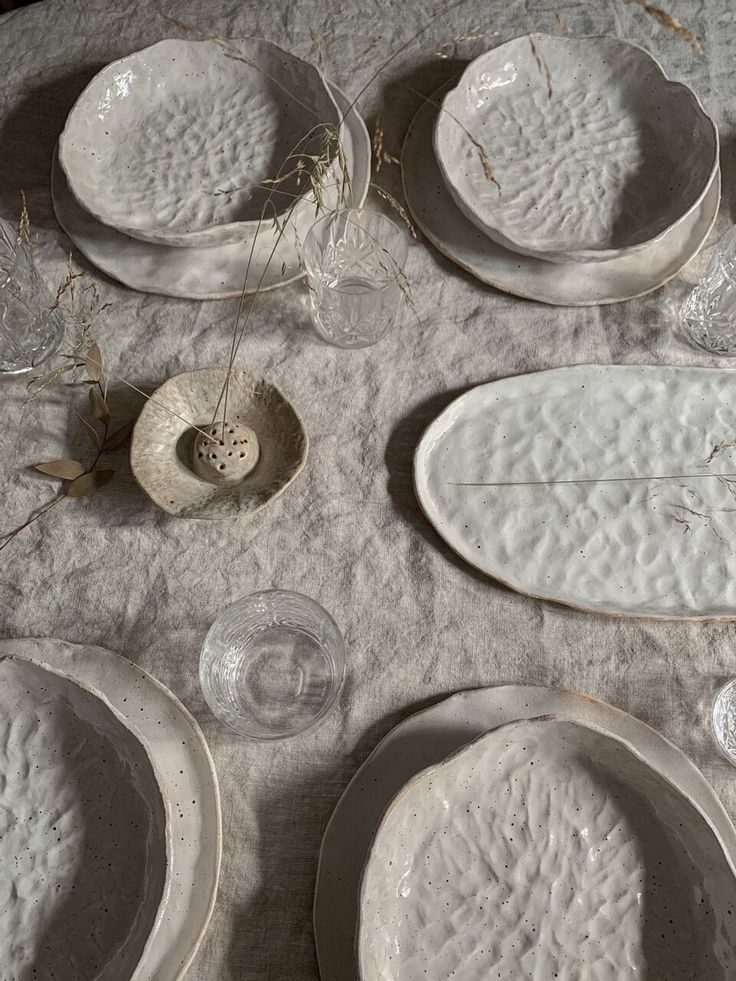 white plates and bowls are laid out on a tablecloth with dried grass in the center