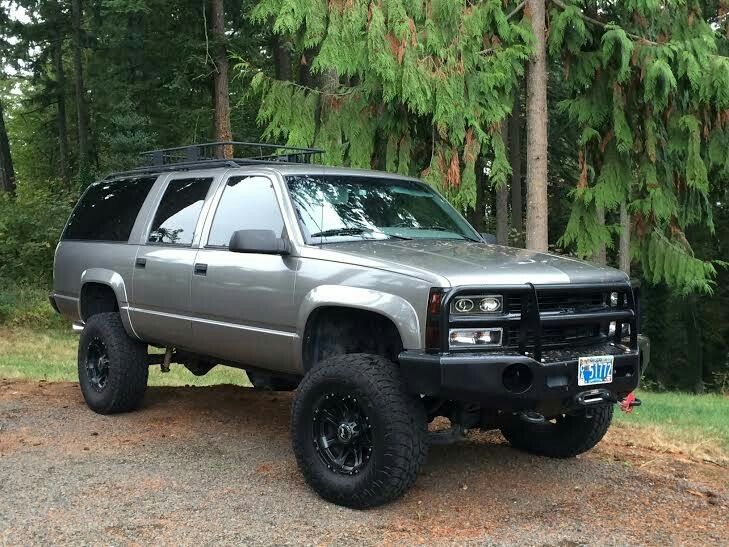 a silver truck parked on top of a dirt road in front of some pine trees