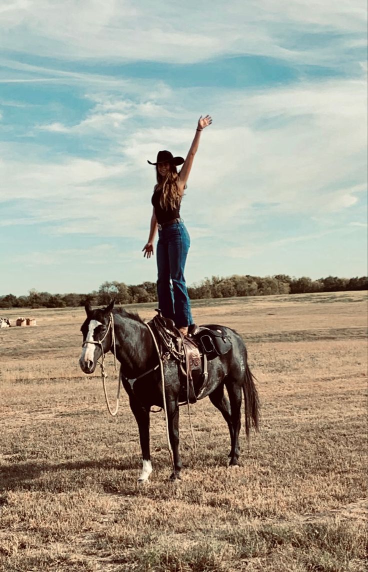 a woman riding on the back of a black horse in a dry grass covered field