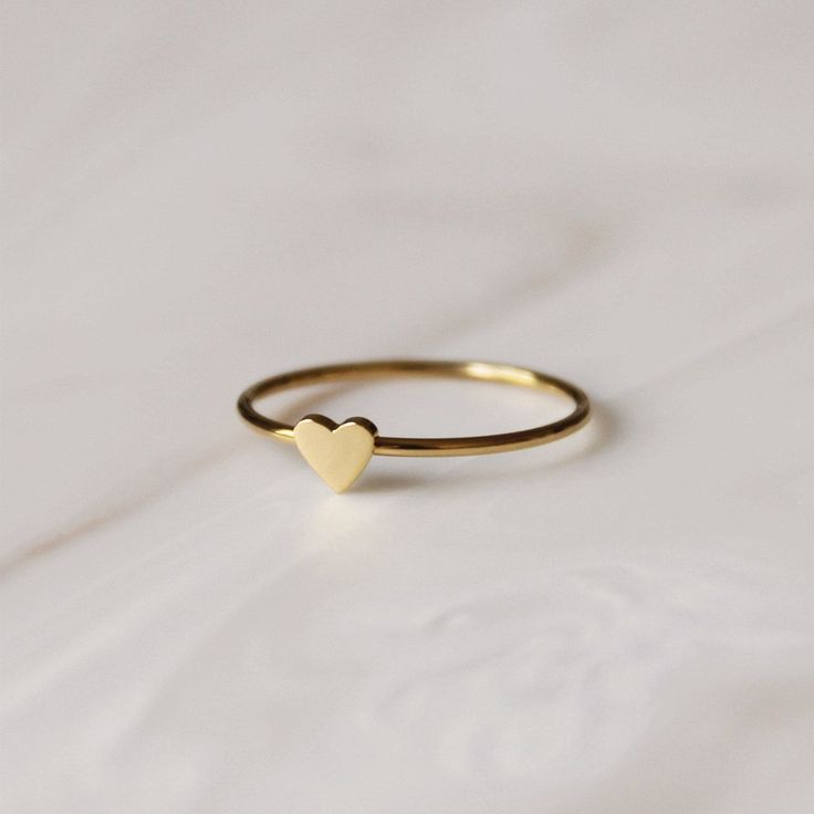 Photo of a thin gold ring with a small gold heart on it sitting on a marble surface. Dainty Stackable Midi Rings For Valentine's Day, Gold Heart-shaped Stackable Midi Rings, Gold Stackable Heart Midi Rings, Dainty Stackable Rings Gift, Dainty Stackable Rings As Gift, Dainty Tiny Heart Ring For Everyday, Dainty Heart Ring For Everyday Wear, Dainty Heart Ring For Everyday, Everyday Stackable Rings For Valentine's Day