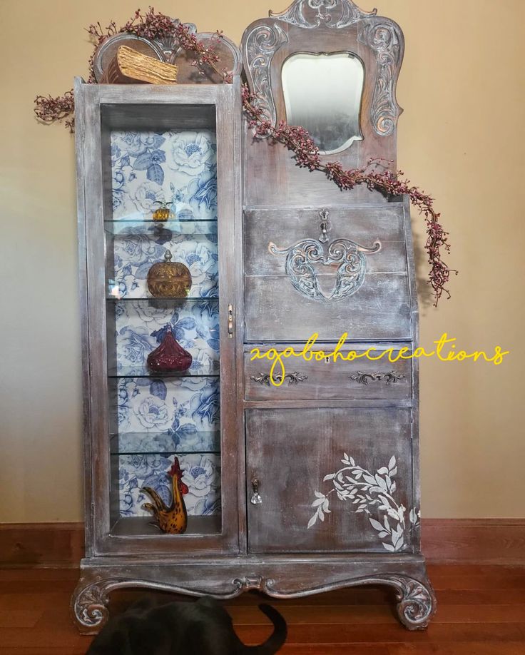 an old china cabinet has been painted with blue and white designs on the doors, along with a black cat