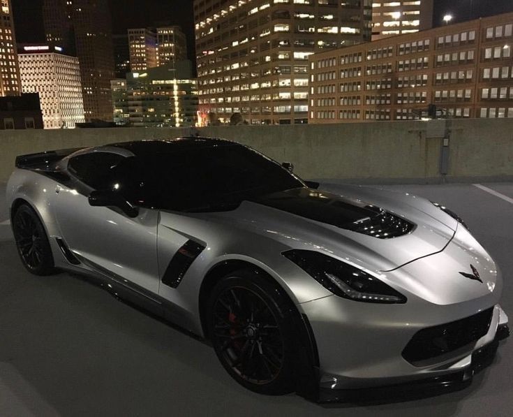 a silver sports car parked in front of some tall buildings at night with lights on