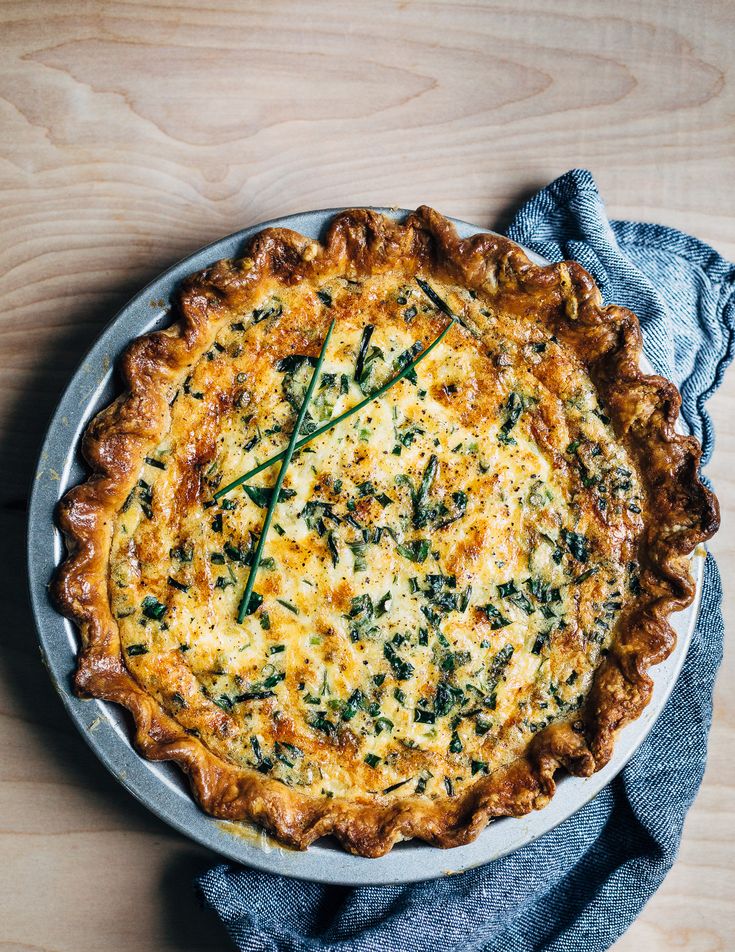 a quiche with cheese and spinach on a plate next to a blue napkin