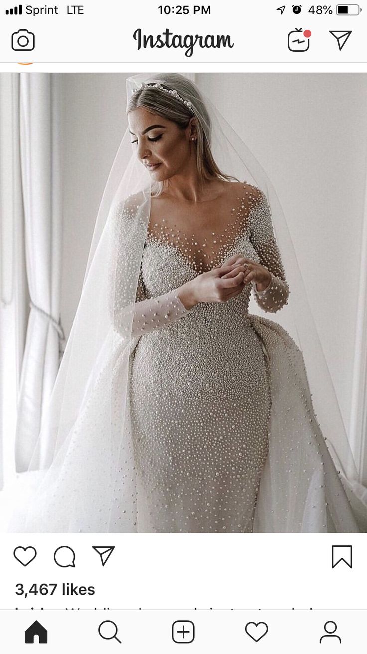 a woman in a wedding dress and veil is looking at her cell phone while wearing a long sleeved gown