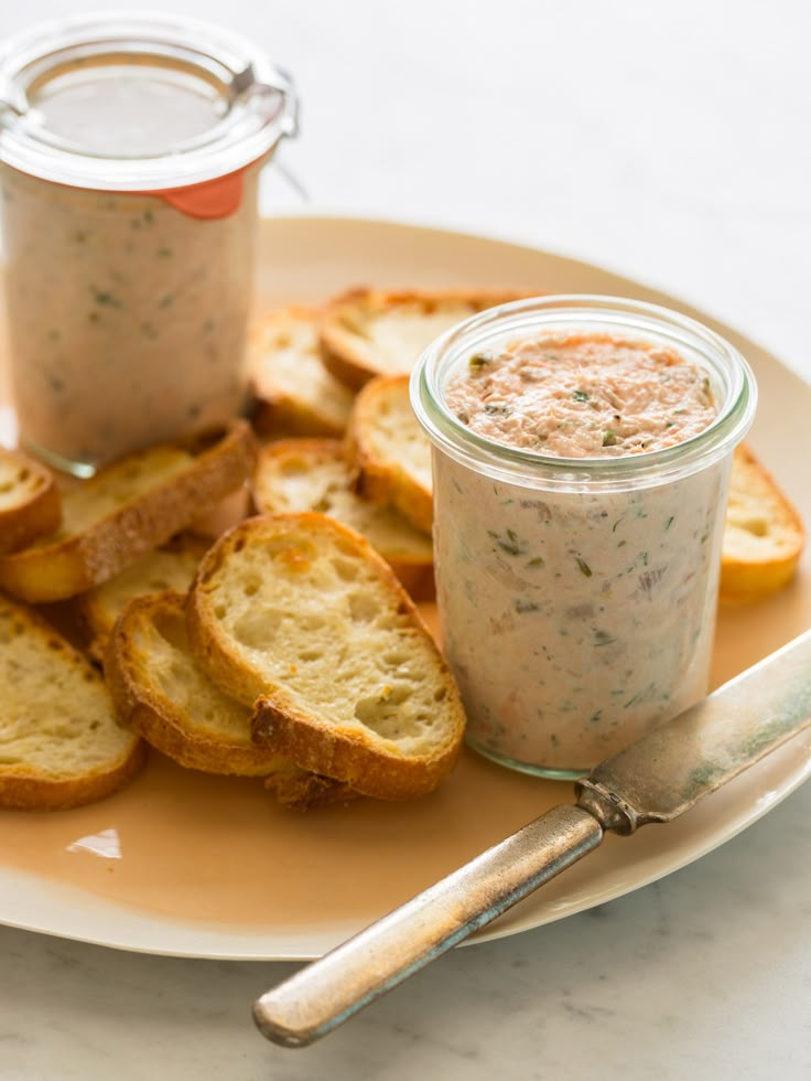 a plate topped with bread slices next to a jar of dip