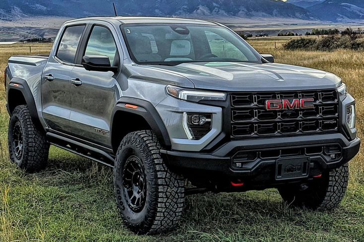 a silver truck is parked in the middle of a field with mountains in the background