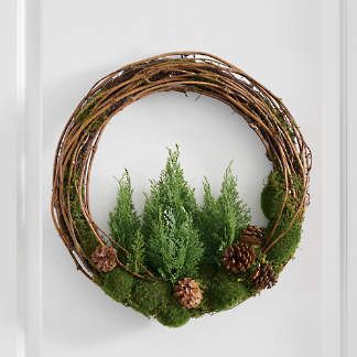 a wreath with moss and pine cones hanging on a door