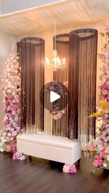 a white bench sitting under two chandeliers in front of pink and yellow flowers