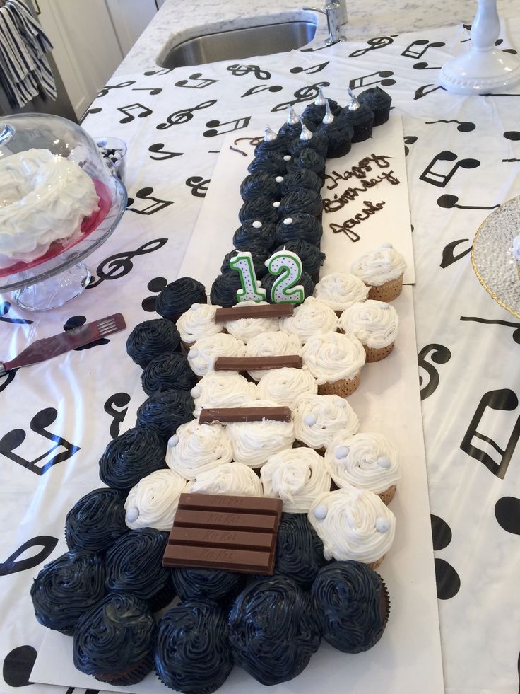 a table topped with cupcakes covered in frosting next to a cake shaped like the number twelve