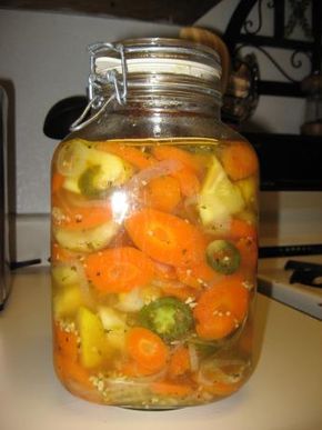 a glass jar filled with pickled vegetables on top of a table next to a microwave