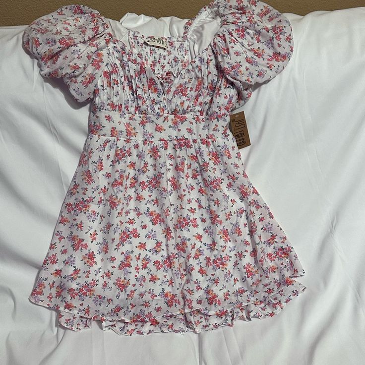 Gorgeous Summertime Vibe Dress With A Beautiful Floral Design Throughout! Short Sleeved Dress With A Couple Of Ties In The Front Of The Chest Area So It Can Be Tied At The Chest Or Left Open. Self Is Made Up Of 65% Polyester And 35% Rayon And The Lining Is 100% Polyester. Measurements Are: Bust 16” Waist 14.5” Hip 23” Flare 33” Waist To Hem 20.5” White Fitted Floral Dress With Puff Sleeves, White Floral Puff Sleeve Dress For Summer, White Floral Puff Sleeve Dress For Garden Party, White Flowy Floral Dress With Square Neck, White Square Neck Floral Dress For Beach, White Square-neck Floral Dress For Beach, Casual White Mini Dress With Square Neck, White Casual Mini Dress With Square Neck, White Floral Puff Sleeve Dress For Spring