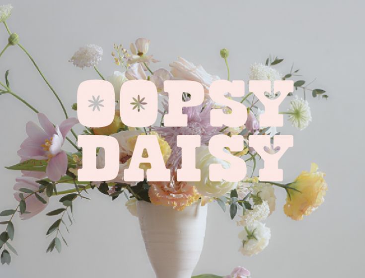 a white vase filled with lots of flowers on top of a table next to the words oopsy daisy