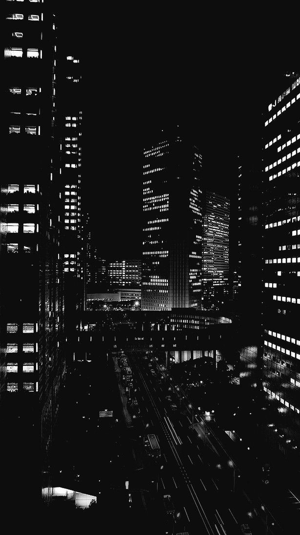 black and white photograph of city at night with lights in the windows, cars on the road