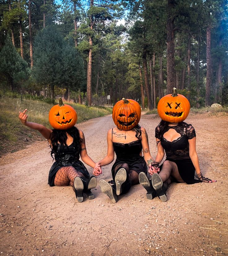 three women sitting on the ground with pumpkins on their heads