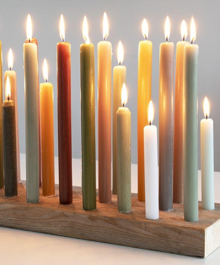 many different colored candles are lined up on a wooden stand with one candle in the middle