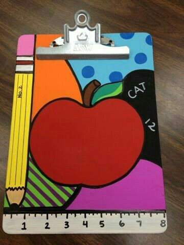 a clipboard with an apple and pencils painted on it, next to a ruler