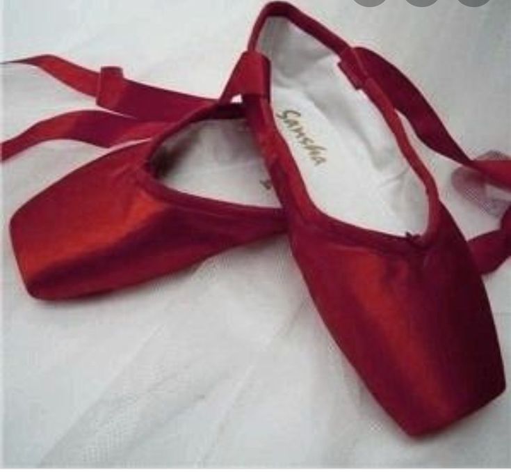 a pair of red ballet shoes sitting on top of a bed